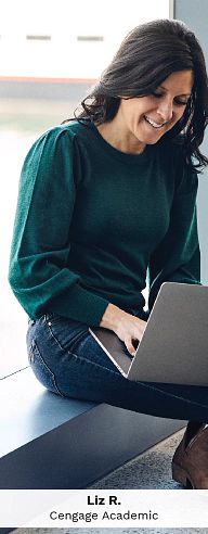 Employee Liz R., Higher Education, types on her laptop in a modern office while working on Cengage's affordability initiatives.